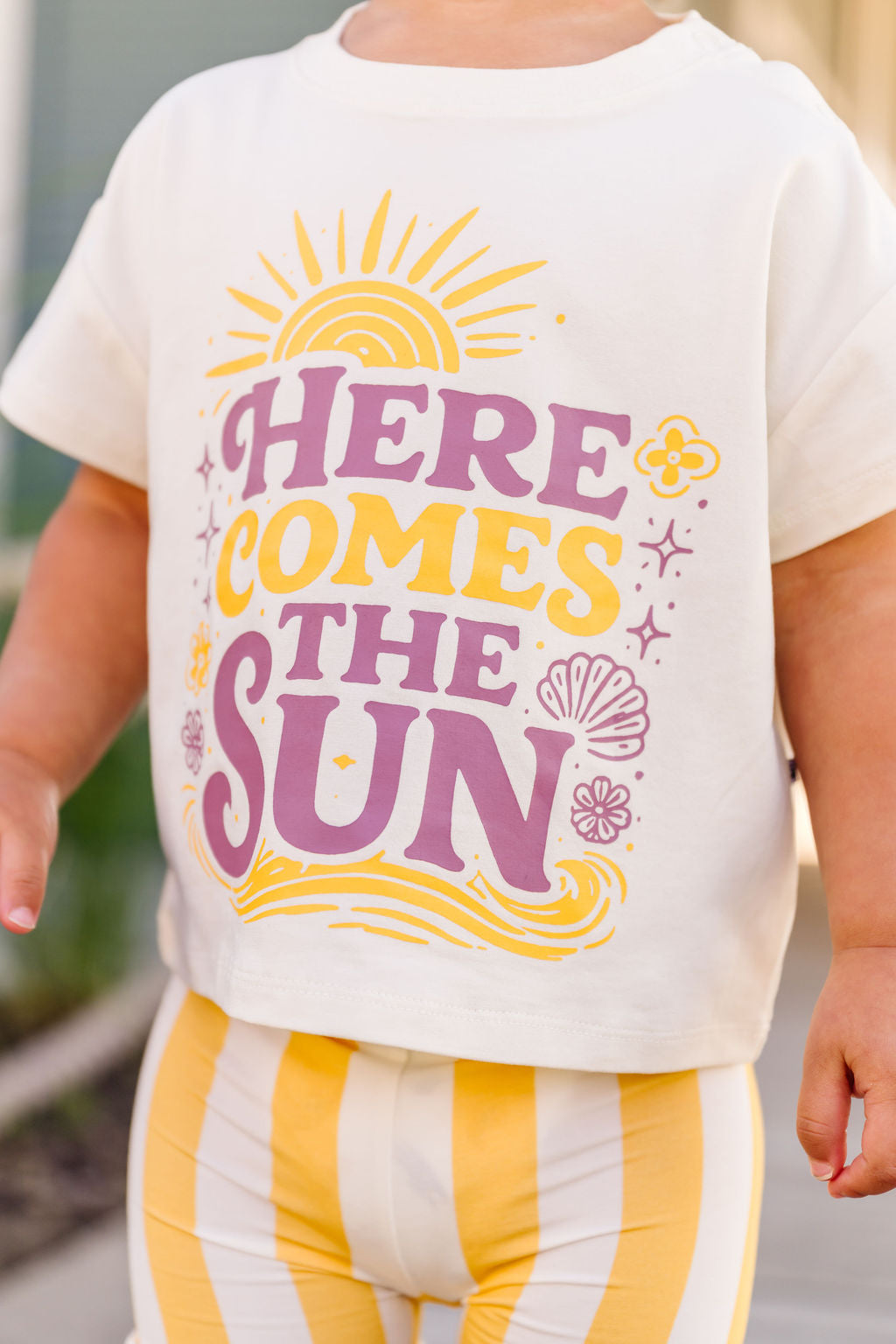 Child wearing a shirt with 'Here Comes the Sun' text and graphics.